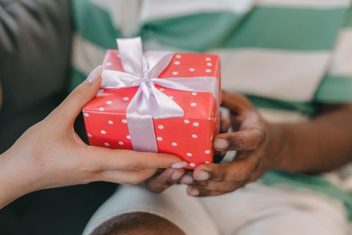 Free A close-up of two hands exchanging a red gift box with a white ribbon indoors. Stock Photo