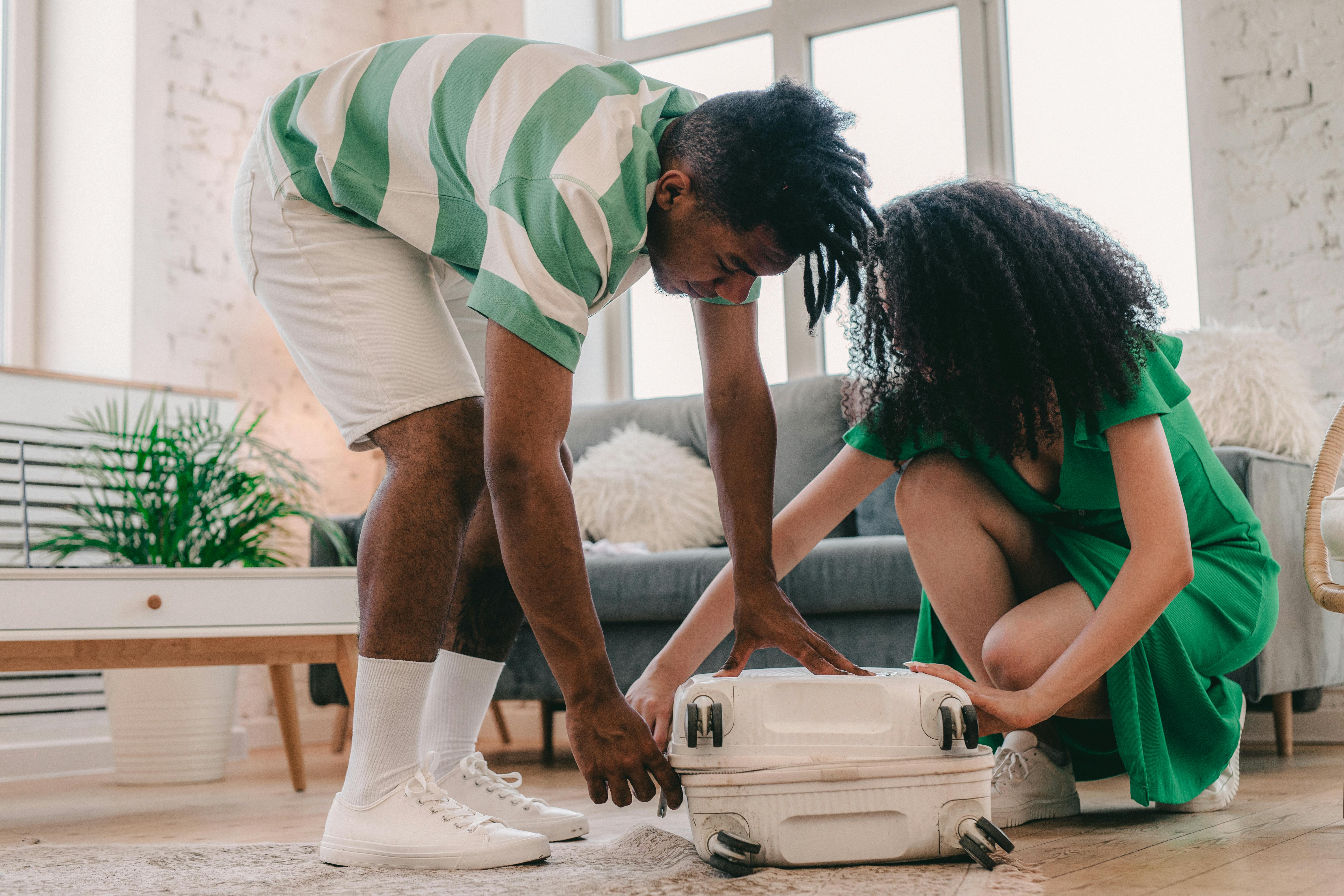 A young couple packing a suitcase in a bright, modern living room, preparing for travel.