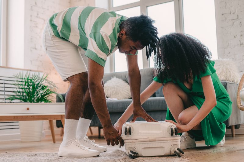 A Black couple kneel on their living-room floor and press a hard-shell rolling suitcase shut. Packing the bag is the moment this guide is about: medications, the insulin cooler and dialysis papers go in first.