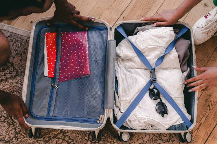 Clothes And Sunglasses In An Open Suitcase On A Rug