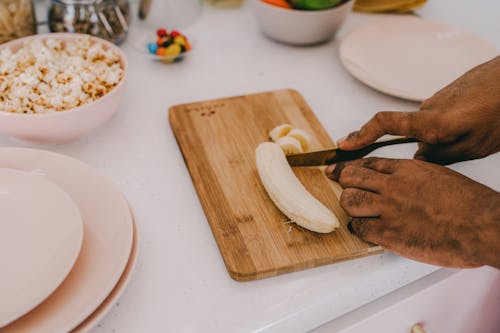 Free Person Slicing a Banana on a Wooden Chopping Board Stock Photo