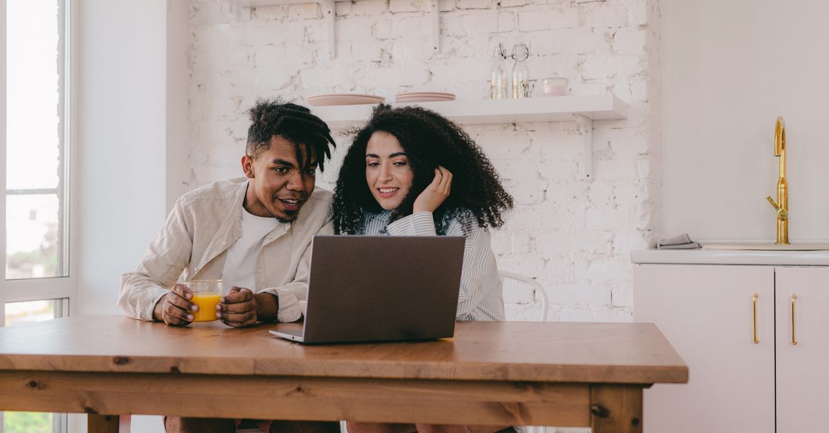 Hispanic couple comparing insurance quotes on laptop at kitchen table