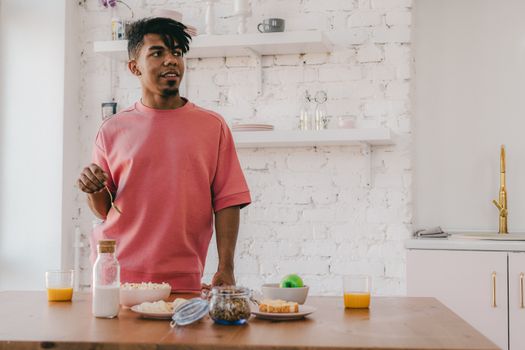A young man making a healthy breakfast with various ingredients in a modern kitchen setting.