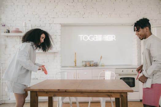 A couple plays table tennis in a cozy kitchen setting with a neon sign reading 'Together' in the background.