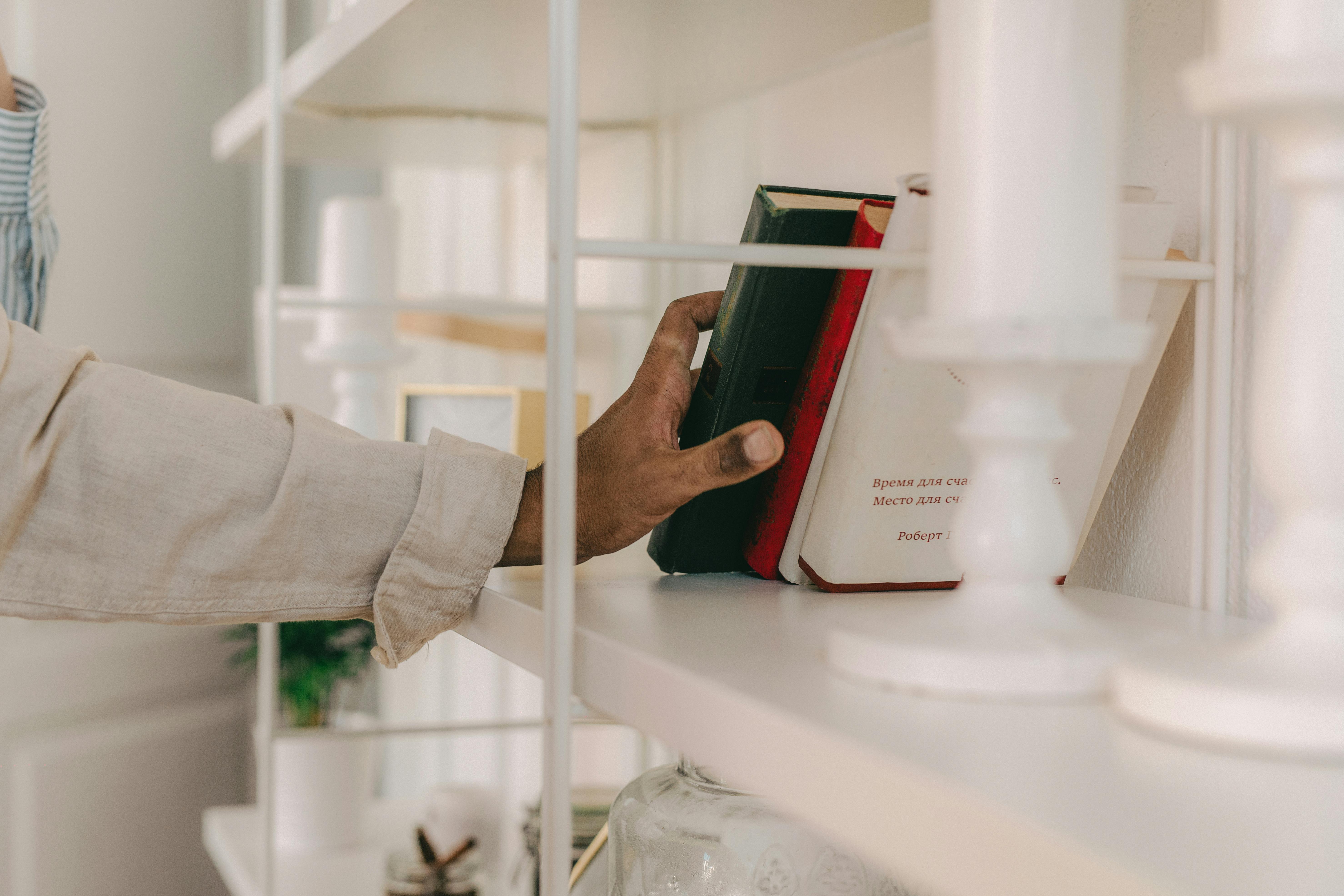 Free Close-up of a hand picking a book from a stylish indoor shelf with soft focus candlesticks. Stock Photo