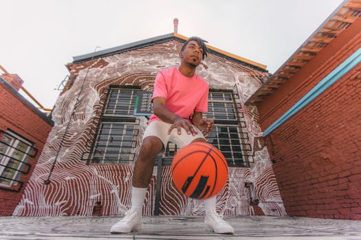 Young man dribbling a basketball in front of a colorful graffiti brick wall, showcasing urban sports culture.