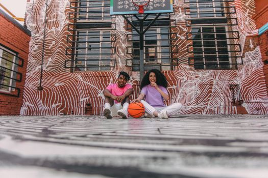 A couple sitting on an urban basketball court, enjoying a sunny day together.
