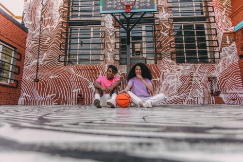 Free A couple sitting on an urban basketball court, enjoying a sunny day together. Stock Photo