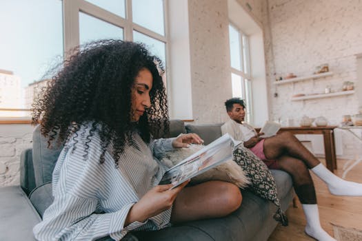A couple relaxing on a sofa, reading books in a bright living room.