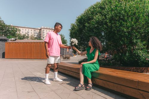 Free Young couple sharing a moment of joy with flowers in a sunny urban setting. Stock Photo
