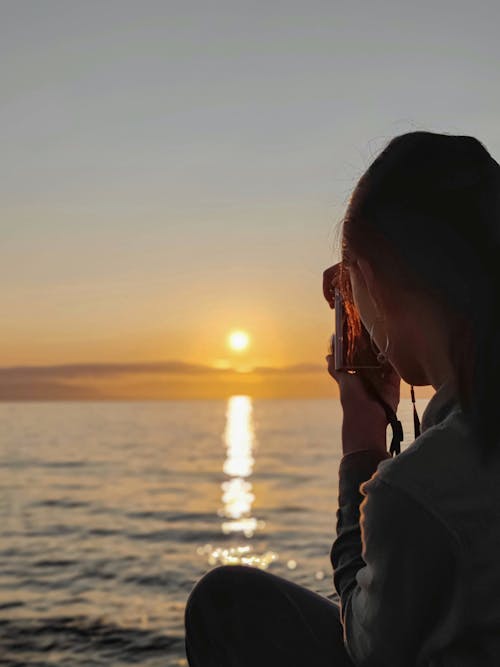 Woman Taking a Picture of a Sunset Over the Sea 
