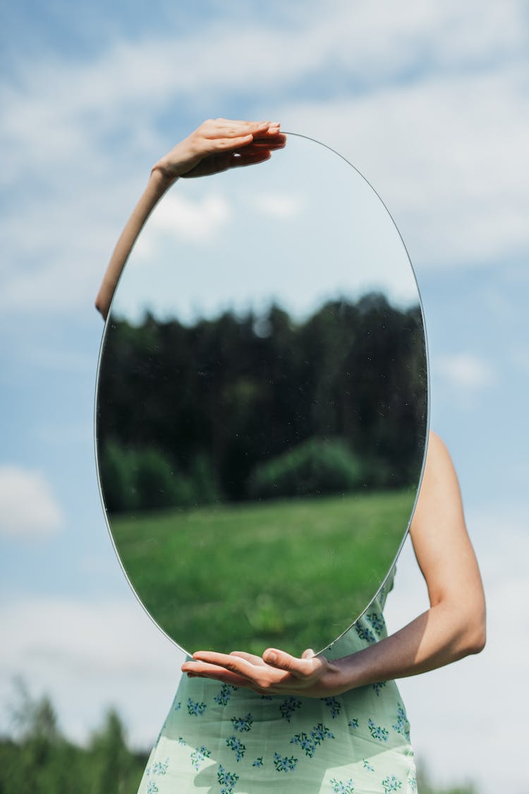 Person In Floral Dress Holding An Oval Mirror 