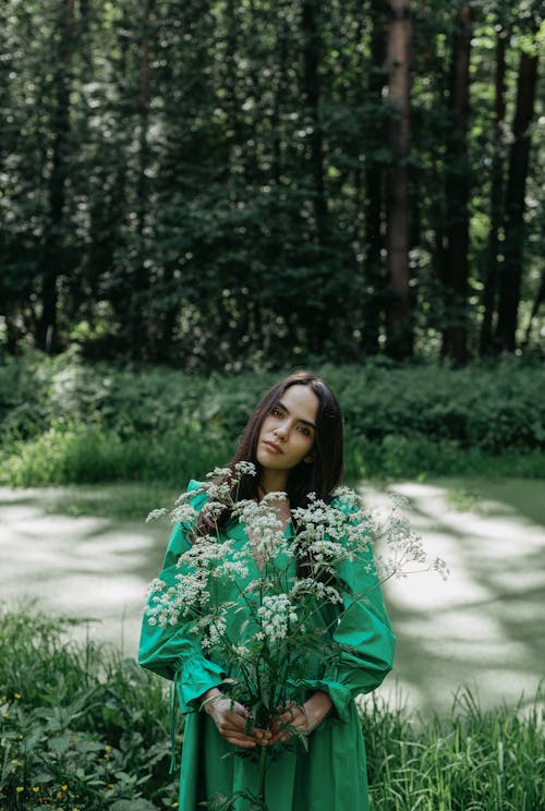 Woman in Green Long Sleeve Dress Holding a Bunch of Flowers 