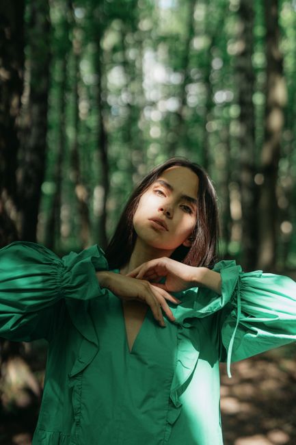 A woman in a green dress poses gracefully in a sunlit forest, creating a serene and natural scene.