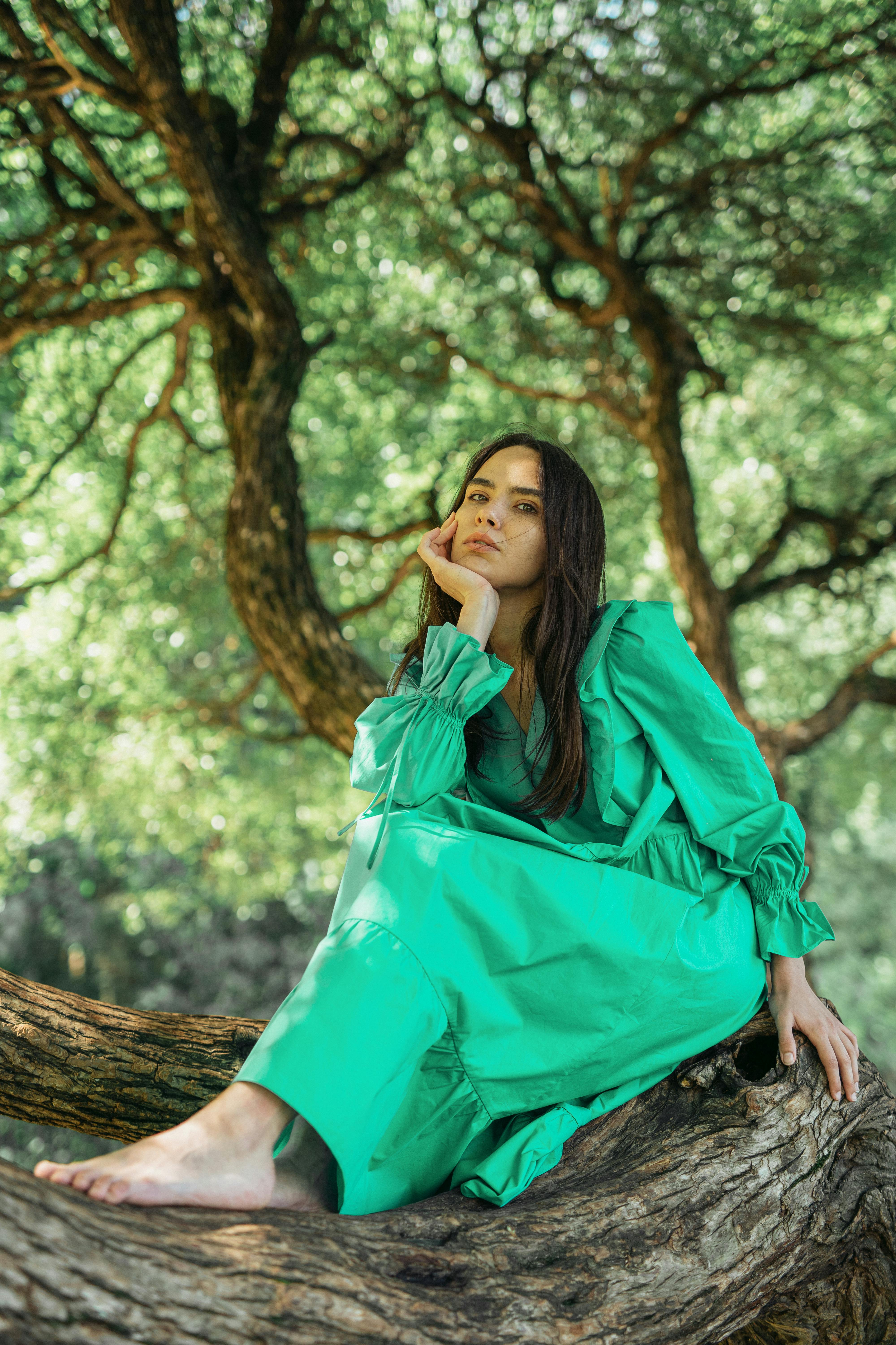 Woman in a vibrant green dress sitting on a tree trunk in a lush forest.
