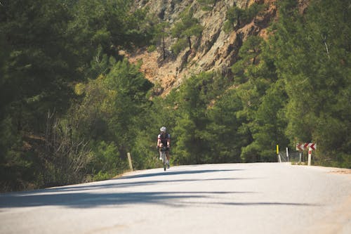 Man in Black Shirt Riding Bicycle on Gray Asphalt Road