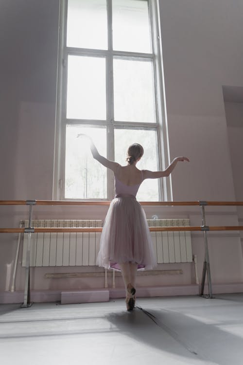 Free Woman in Pink Dress Standing beside Brown Ballet Bars Stock Photo