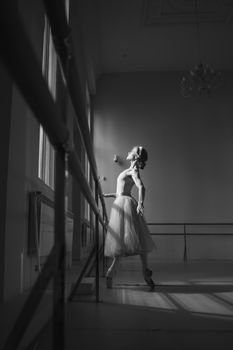 Graceful ballerina practicing ballet at barre in a studio, captured in black and white.