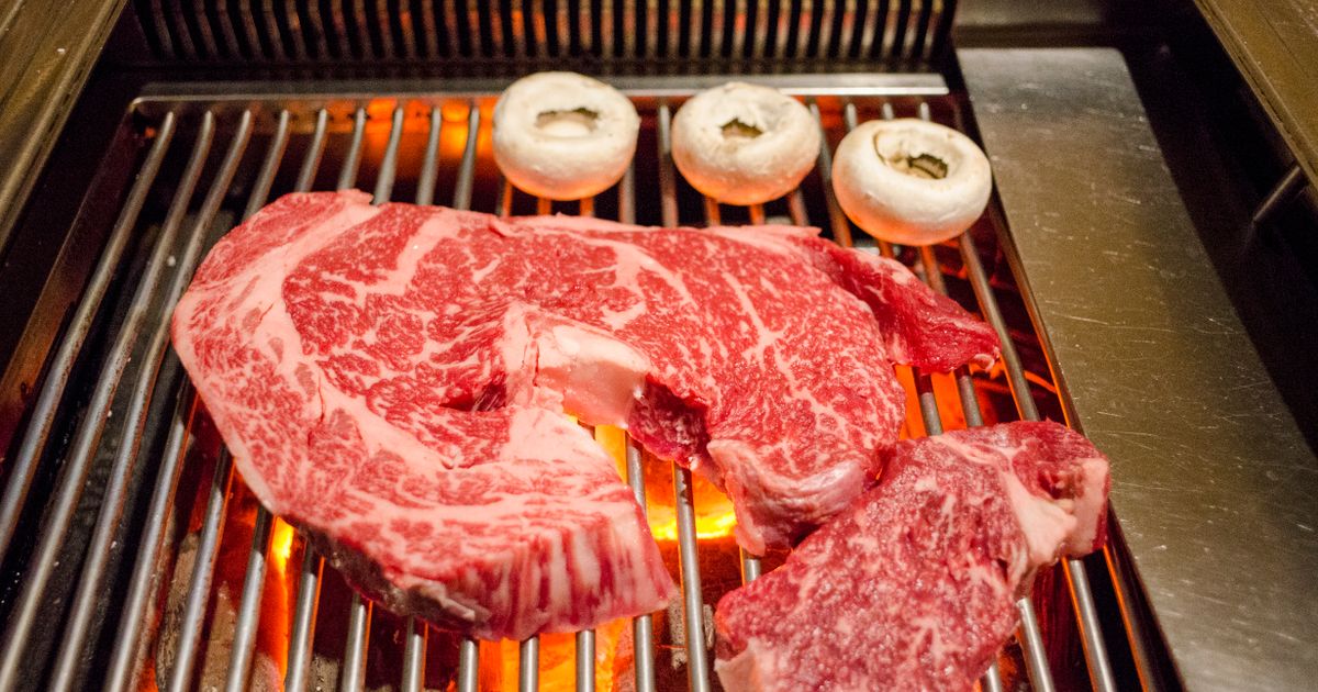 Close-up of Wagyu beef steaks sizzling on a grill showing dense marbling and grill marks