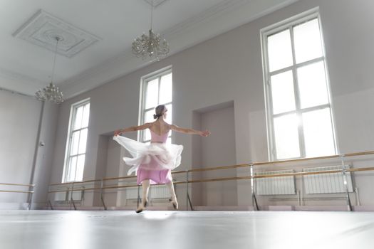 A graceful ballerina practicing ballet movements in a bright, sunlit dance studio.