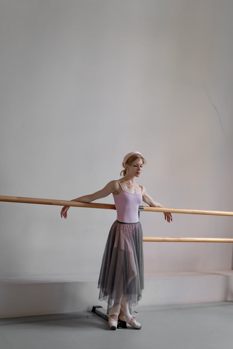 A Ballerina Leaning On A Barre While Looking Down