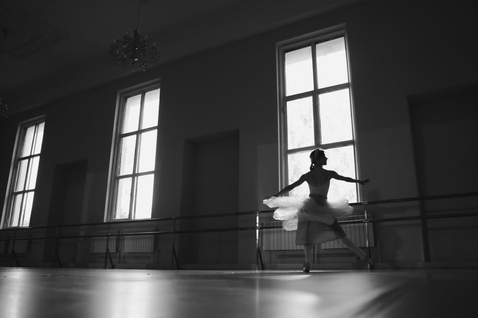 バレリーナが美しく照らされたグレースケールのスタジオでダンスの動きを完璧にしています。