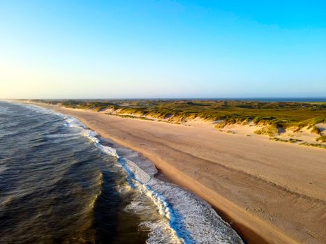 Stunning aerial shot of Hvide Sande beach with vast shoreline and calm waves under a clear blue sky.