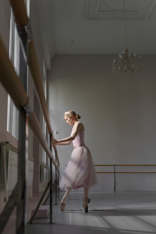 Free A serene ballerina practices at the barre in a light-filled ballet studio. Stock Photo