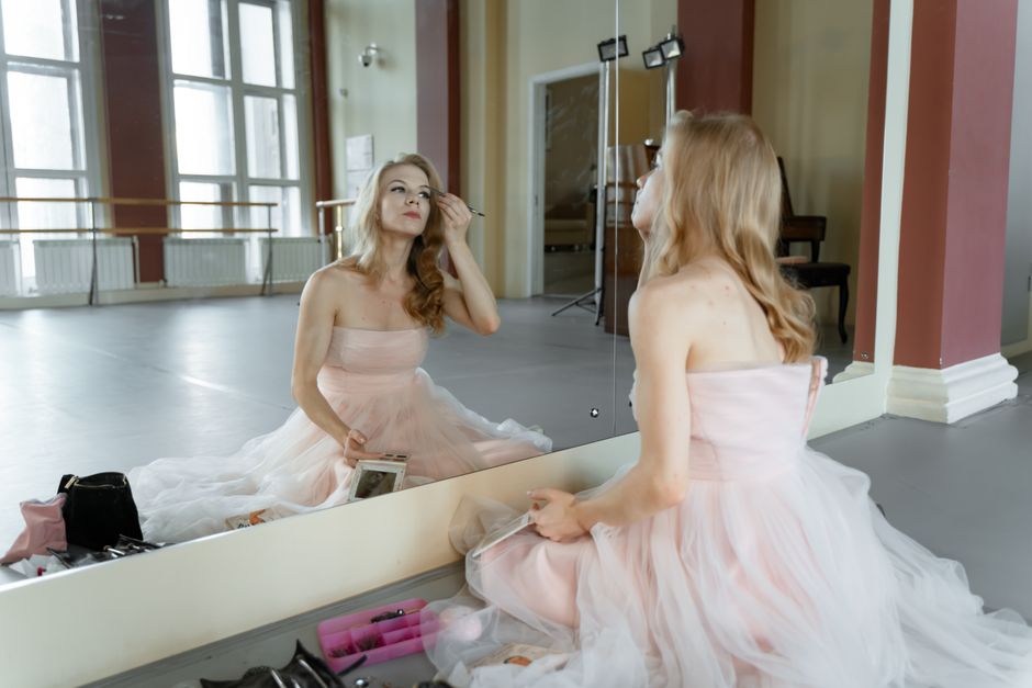 Ballet dancer in a studio, preparing with makeup in front of a mirror.