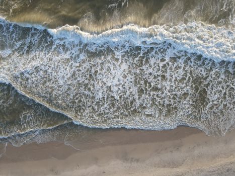 Stunning aerial view of ocean waves crashing onto the sandy shores of Hvide Sande, Denmark.