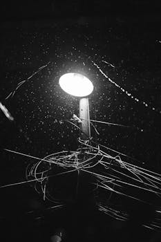 A captivating black and white photo of a streetlight illuminating wires and raindrops at night.