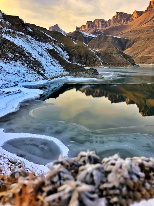 Free Serene winter view of a frozen lake surrounded by mountains reflecting in icy waters. Stock Photo