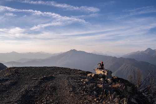 A Person Sitting on a Rock at a Mountain Peak