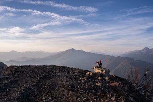 Free A person sits on a mountain peak, admiring the expansive view of distant mountains under a blue sky. Stock Photo