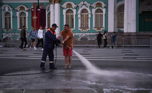Free Two workers using a hose to clean an urban street, in front of a historic building. Stock Photo