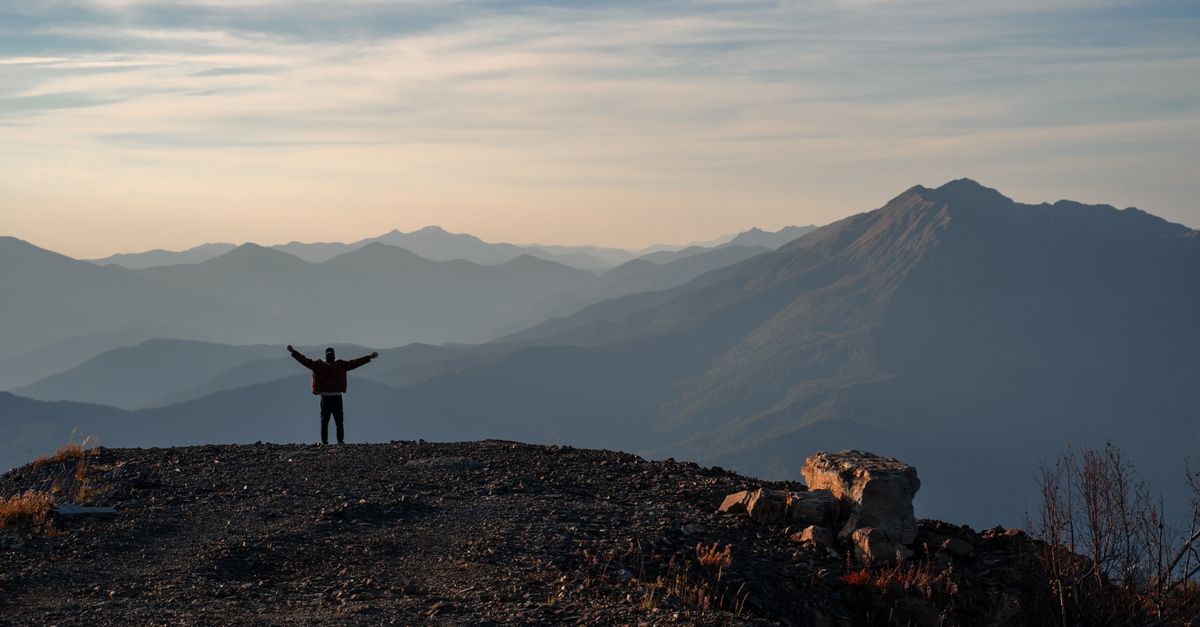 silhouette of a person standing on a mountain peak at sunrise looking at the horizon