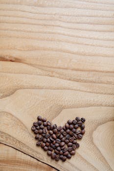 A heart shape made with coffee beans on a textured wooden surface. Ideal for coffee-themed content.