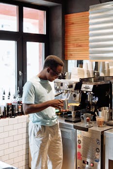 Barista in light attire making coffee at espresso machine in a chic, well-lit café.
