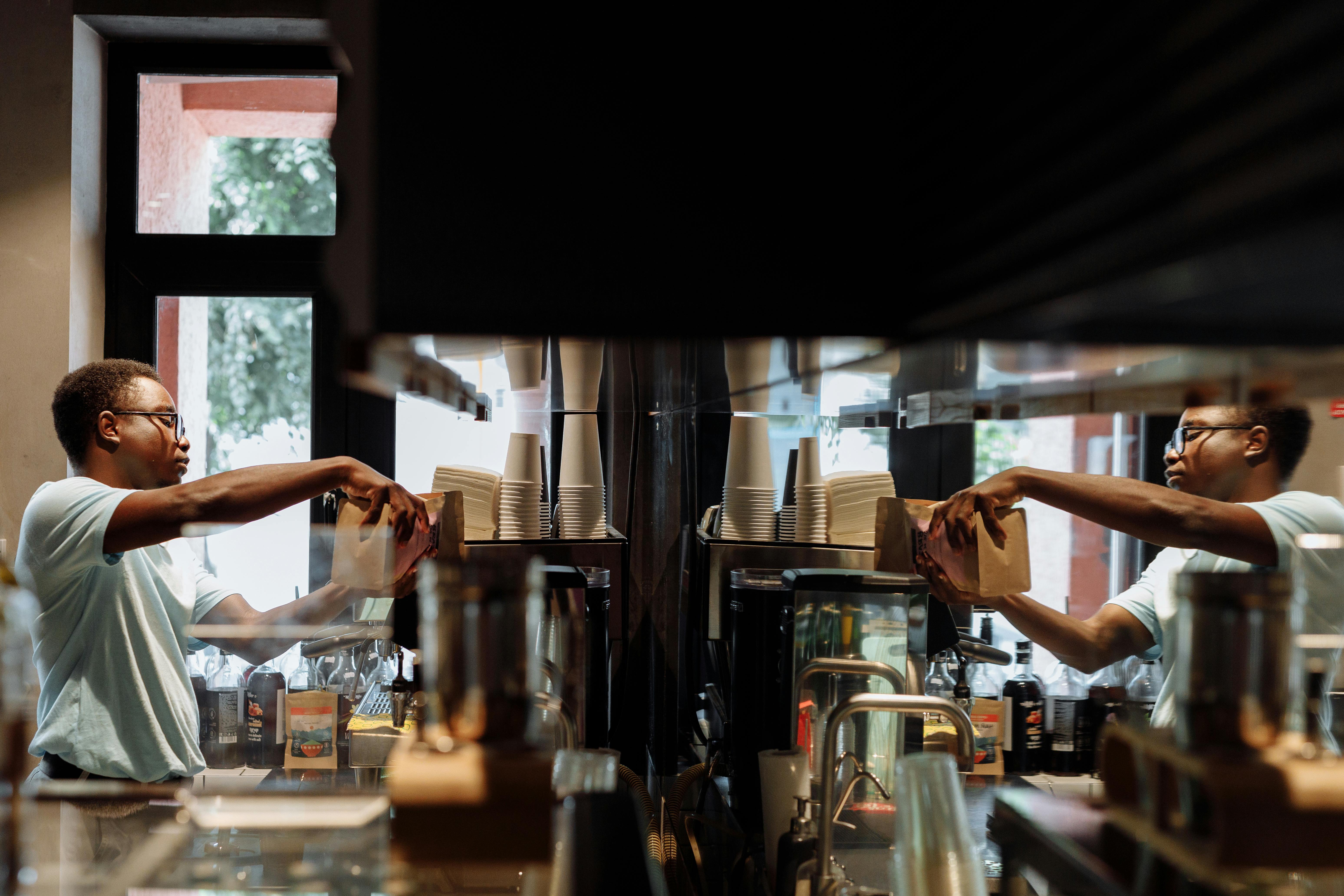 A Man Holding Brown Paper Bag in Front of Espresso Machine