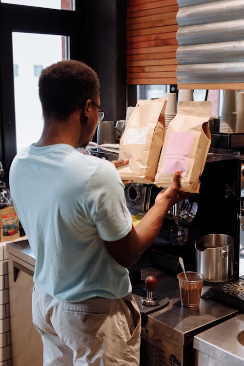 A Man Standing Near Coffee Machine Holding Brown Paper Bags