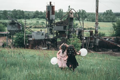 Free Two children in gas masks hold balloons near an old industrial plant, symbolizing innocence amidst pollution. Stock Photo