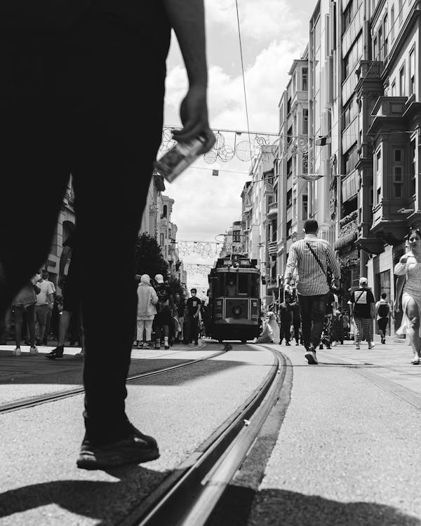 Grayscale Photo of Person in Black Pants Standing on the Tramway