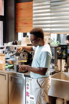 Barista in a coffee shop pouring milk into a cup, enhancing the coffee experience indoors.