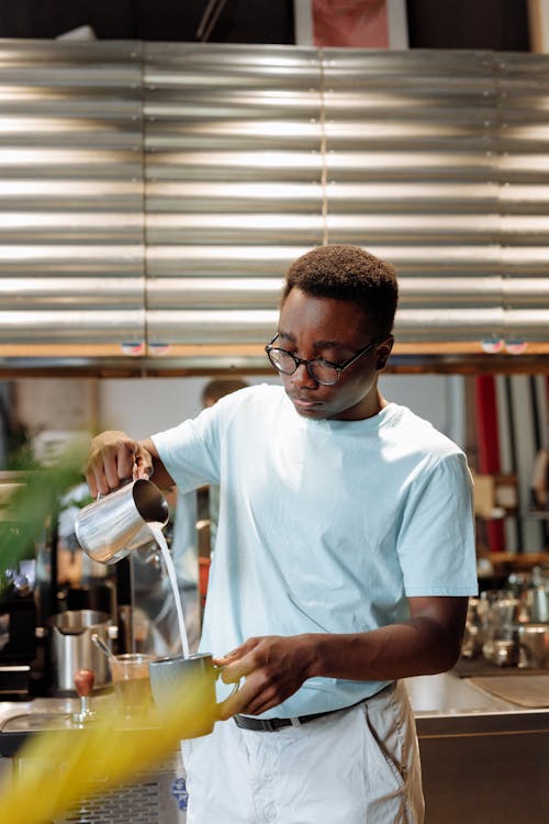 Man in White Crew Neck T-shirt Holding a Ceramic Mug and a Pitcher