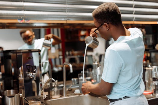 Barista expertly pouring milk into coffee with a frothing jug in a coffee shop setting.