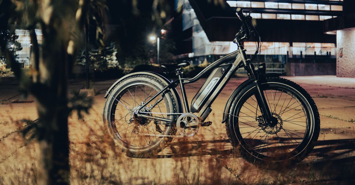 Photo by Erik Mclean A sleek electric bike is parked on a city pavement, illuminated by streetlights at night.