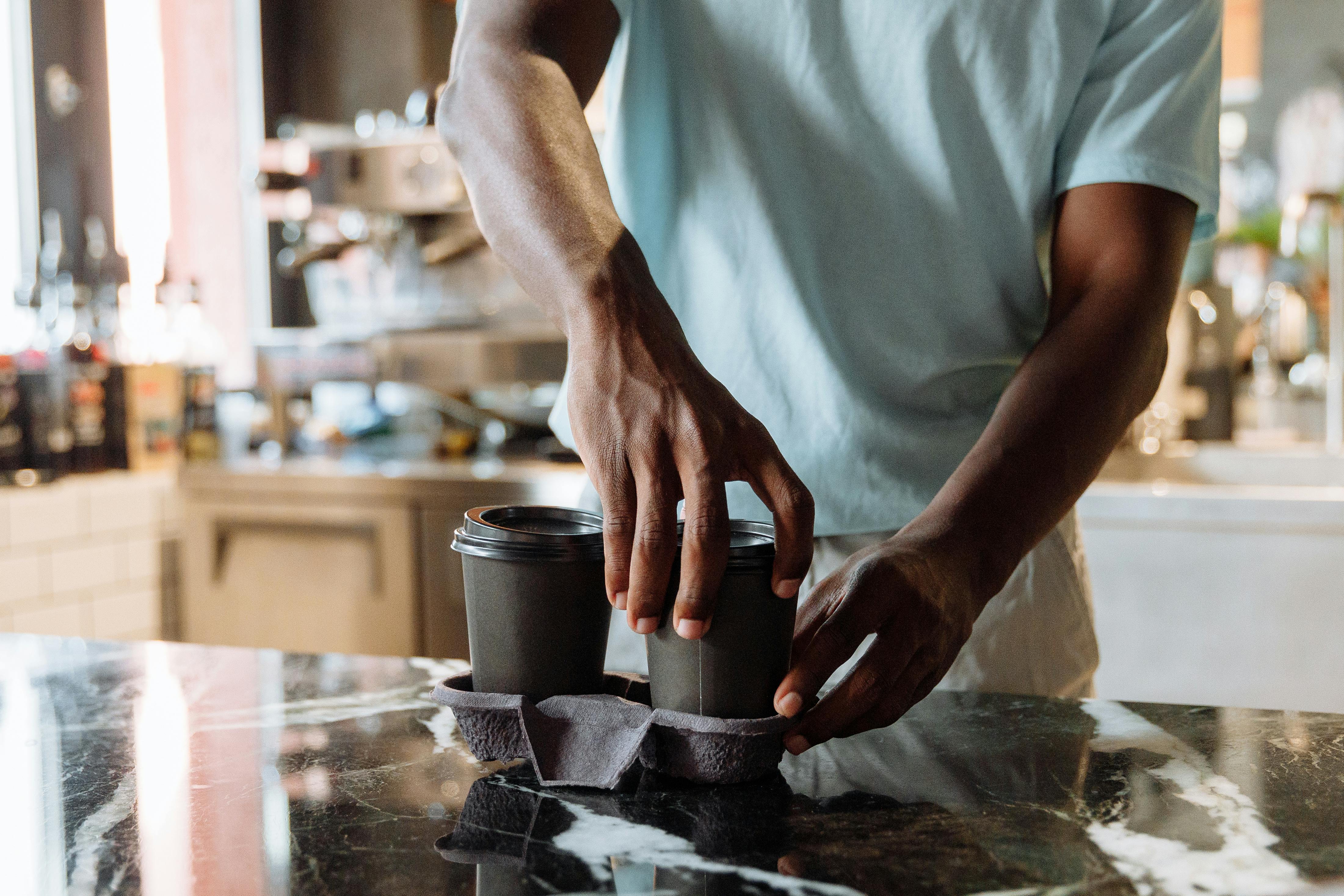 Close-up of a barista handling take-out coffee cups on a marble counter inside a cafe.