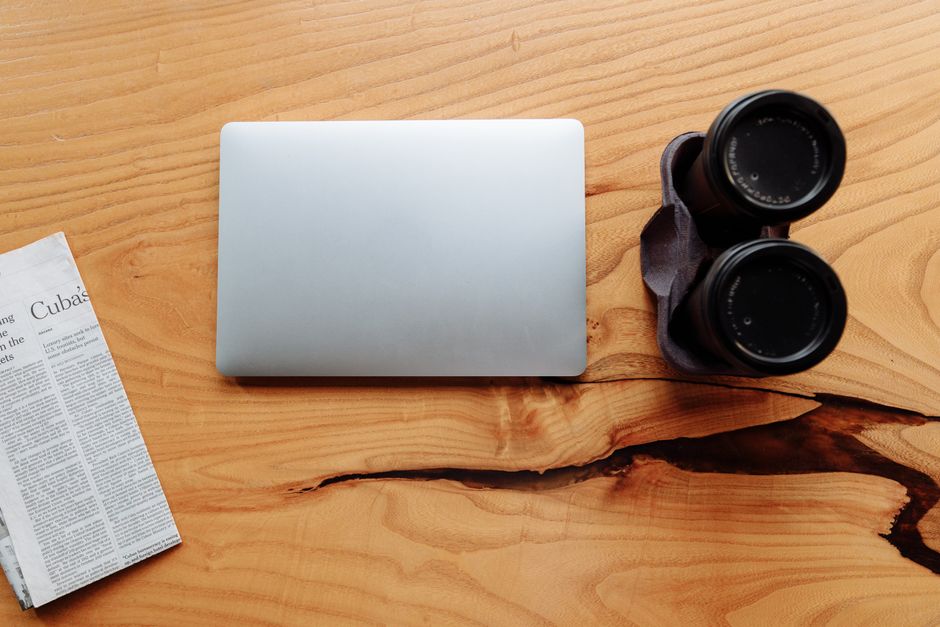 Flat lay of binoculars, laptop, and newspaper on a wooden table. Perfect for work and exploration themes.