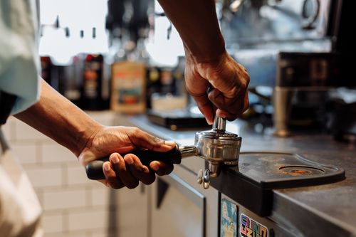 Free Close-up of a barista using a tamper on a portafilter in a coffee shop setting. Stock Photo