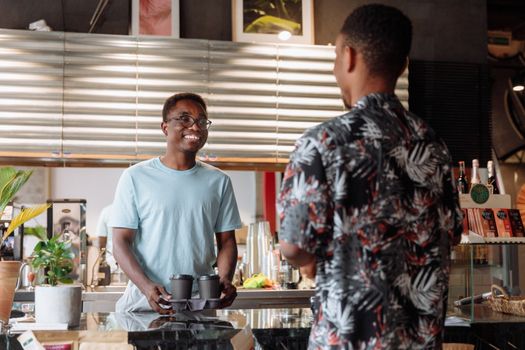 Smiling barista serves coffee to customer at lively urban cafe.